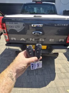2 Ford Ranger keys being held up in front of rear of black pick up truck in Darlington